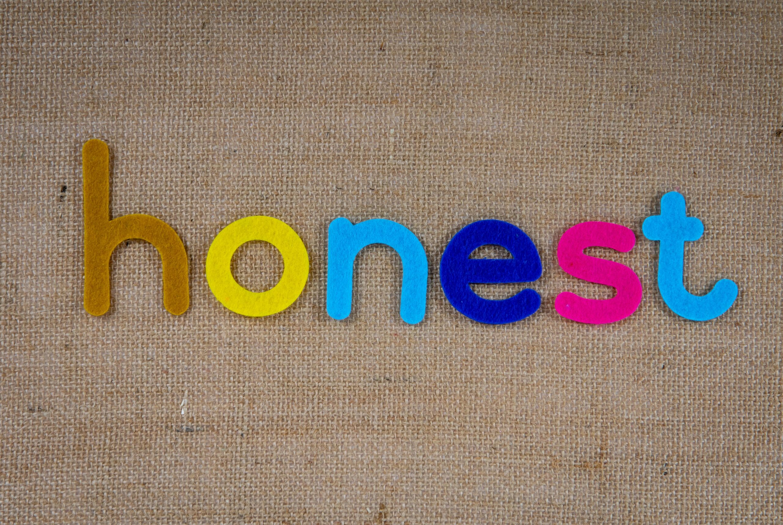 Bright felt letters spelling 'honest' on natural burlap background.